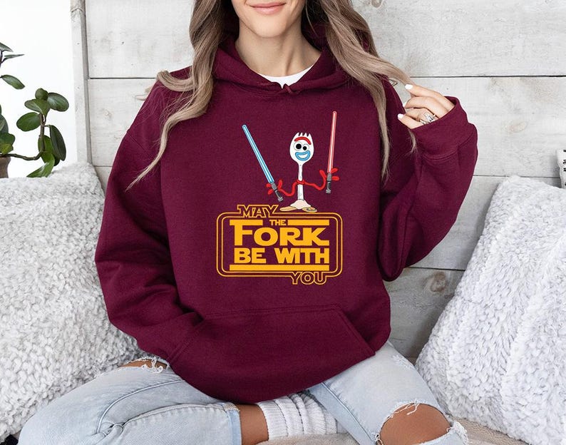 Op de afbeelding: Een bordeauxrode hoodie met een afbeelding van een witte spork die een blauw en een rood lichtzwaard vasthoudt. Onder het figuur staat de gele tekst MAY THE FORK BE WITH YOU, in een rechthoekig kader met afgeronde hoeken.