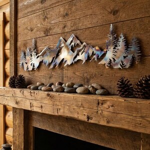 May include: A rustic fireplace mantel with a metal mountain range wall art. The art piece is mounted above the mantel, which is decorated with river rocks and pine cones. A vintage lantern sits on the hearth.