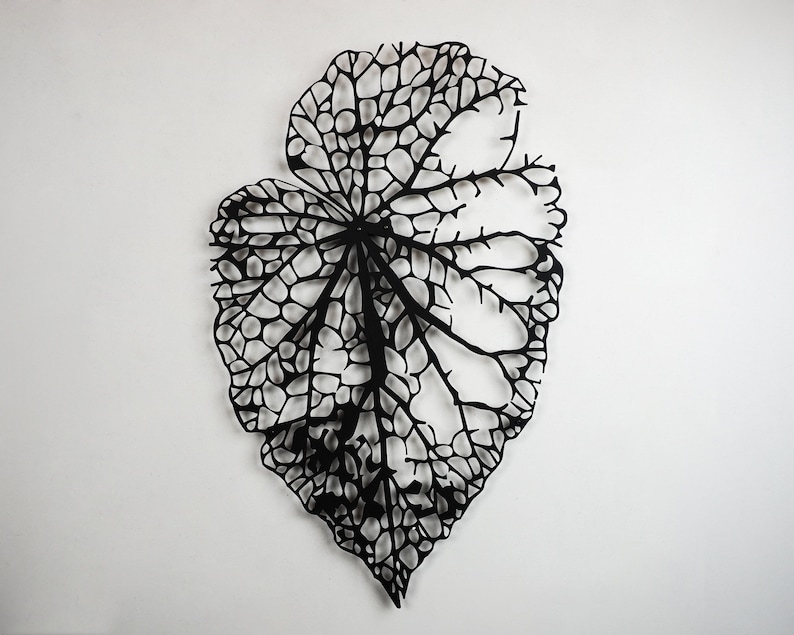 Puede incluir: Una gran pieza de arte mural en forma de hoja negra. La hoja tiene un dise&ntilde;o intrincado y calado, con una red de venas y c&eacute;lulas. La obra de arte est&aacute; montada en una pared blanca, creando un contraste llamativo.