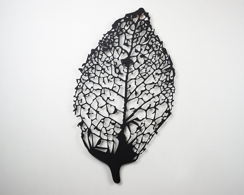 Puede incluir: Escultura de hoja negra estilizada con intrincados cortes en forma de venas. La forma de la hoja es alargada y detallada, mostrando un dise&ntilde;o calado delicado. La obra de arte est&aacute; montada sobre un fondo blanco, resaltando el contraste.