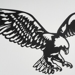 Op de afbeelding: Zwarte metalen wanddecoratie van een adelaar met uitgespreide vleugels. De adelaar is in vlucht en heeft een gedetailleerd ontwerp.