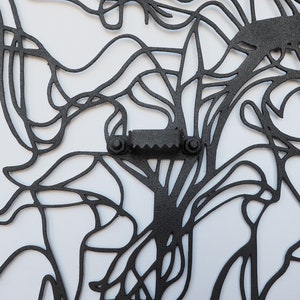 May include: Black metal wall art with an abstract design of interconnected lines and shapes. The artwork features a sawtooth hanger for easy mounting. The design is intricate and appears to be cut from a single sheet of metal.