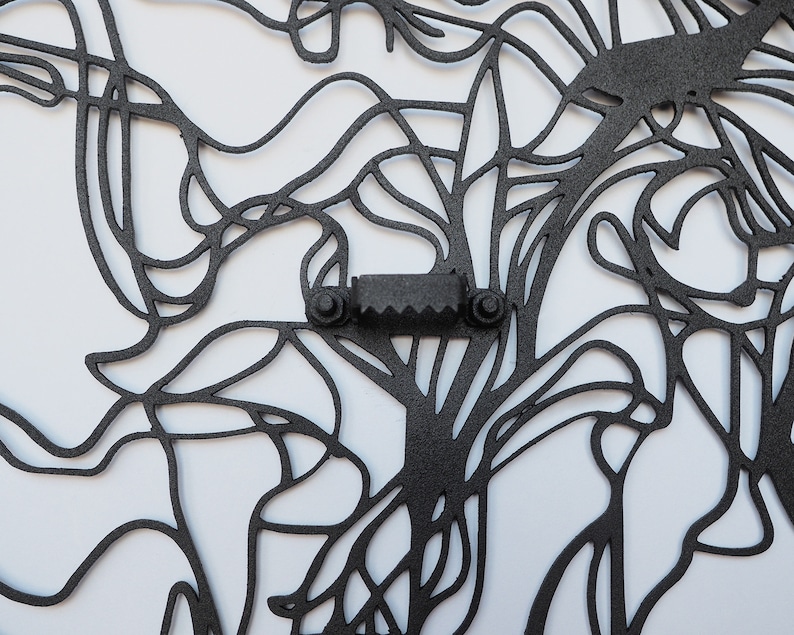 May include: Black metal wall art with an abstract design of interconnected lines and shapes. The artwork features a sawtooth hanger for easy mounting. The design is intricate and appears to be cut from a single sheet of metal.