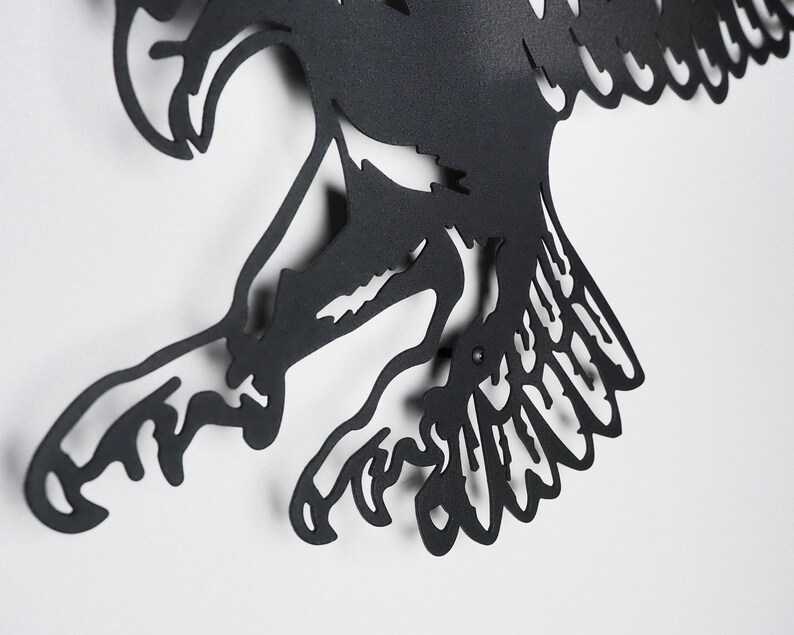 Op de afbeelding: Zwarte metalen wandkunst met een gestileerde vogel in vlucht. De vogel heeft gedetailleerde vleugels en klauwen.