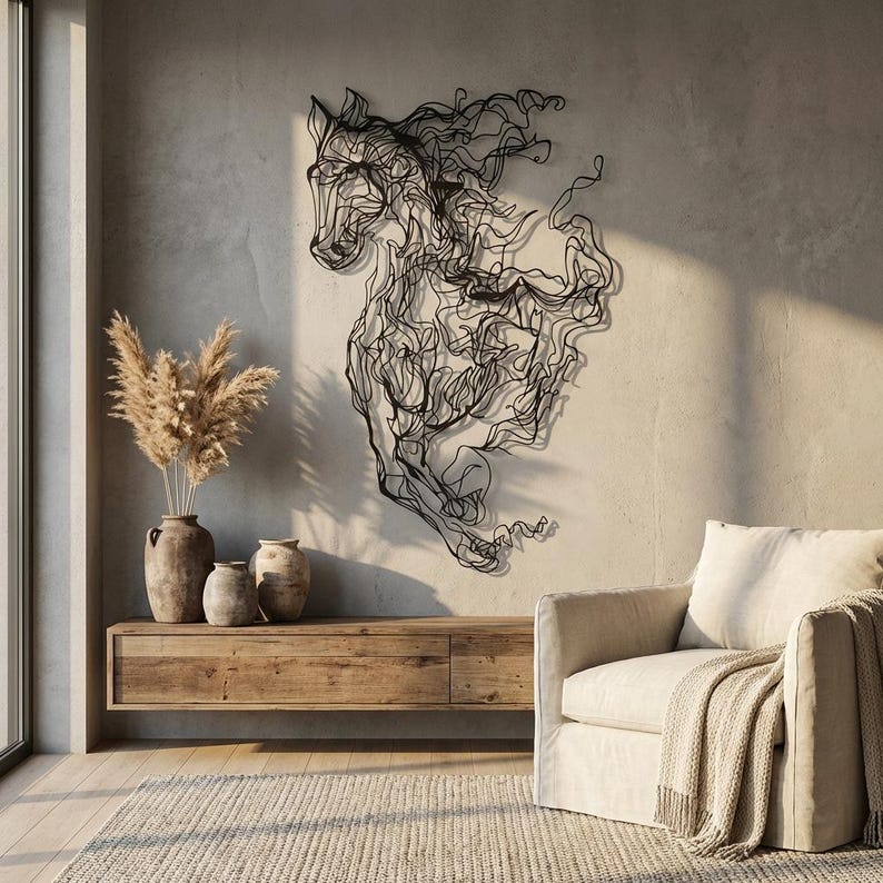 May include: A black metal horse wall art sculpture. The artwork is a stylized representation of a horse, with flowing lines creating the mane and body. The sculpture is mounted on a light gray wall, with a wooden cabinet and beige armchair in the background.