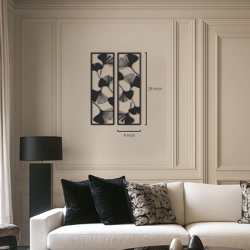 May include: Two black metal wall art panels, each 9 inches wide and 29 inches tall, featuring a ginkgo leaf design. The panels are displayed on a beige wall above a white sofa with black pillows.