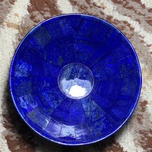 Op de afbeelding: Een blauwe lapis lazuli kom met een mozaïekontwerp. De kom is gemaakt van veel kleine stukjes lapis lazuli die in een cirkelvormig patroon zijn gerangschikt. De kom is gepolijst en heeft een glanzende afwerking.