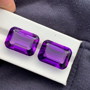 May include: Two deep purple amethyst gemstones cut in a rectangular emerald shape.