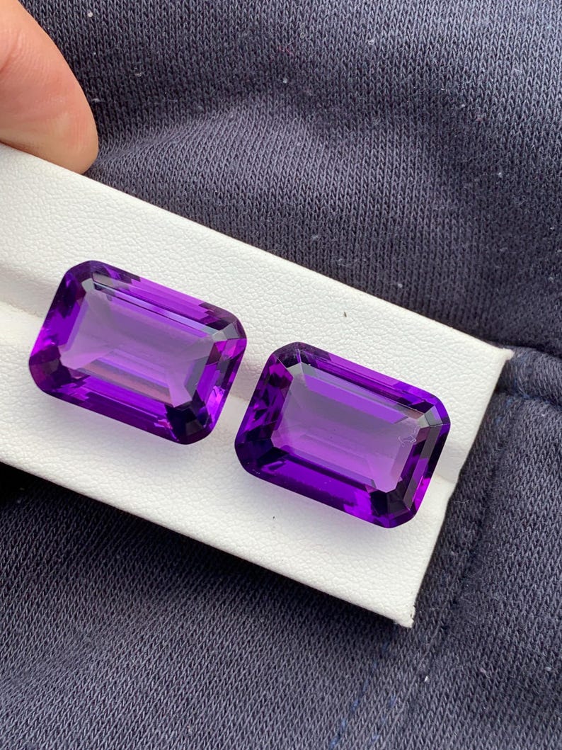 May include: Two deep purple amethyst gemstones cut in a rectangular emerald shape.