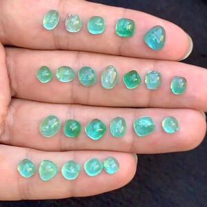 May include: A selection of small, polished gemstones in shades of green and teal. The gemstones are displayed on a light surface, highlighting their clarity and colour variations. The stones are of different sizes and shapes, with a variety of cuts.