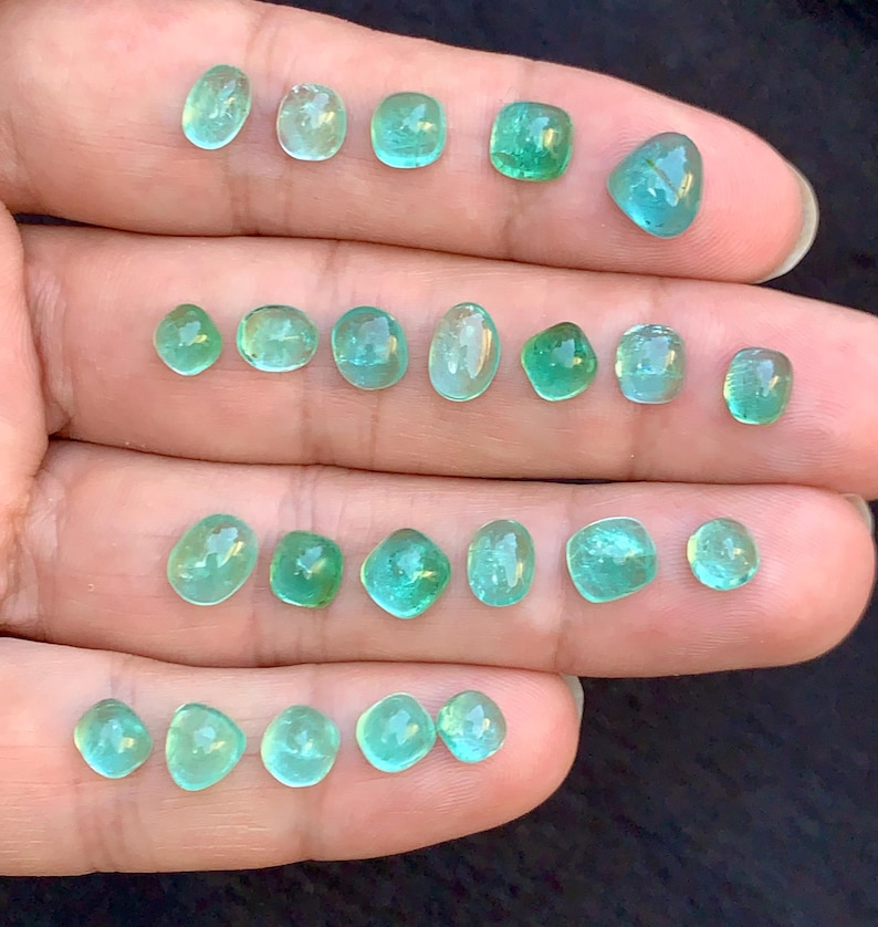 May include: A selection of small, polished gemstones in shades of green and teal. The gemstones are displayed on a light surface, highlighting their clarity and colour variations. The stones are of different sizes and shapes, with a variety of cuts.
