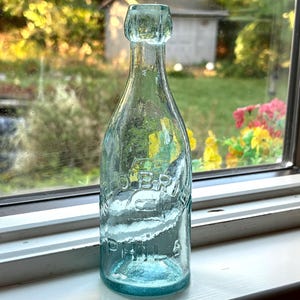 May include: A vintage light blue glass bottle with a rounded top and a narrow neck. The glass features embossed lettering that reads "OBR" and "PHILA" on the front surface. The bottle has a smooth, translucent finish and a cylindrical body.