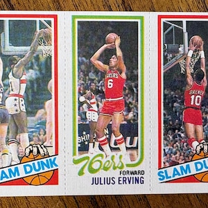 May include: Vintage basketball trading card featuring three panels. The panels depict players in action, including Julius Erving of the 76ers. The cards have a red, green, and white color scheme with the words "SLAM DUNK" and "76ers" visible.