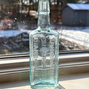 May include: A clear glass bottle with a textured surface. The bottle is embossed with the text "FERROUS SULPHATE" and "DIAMOND" in a rectangular shape.