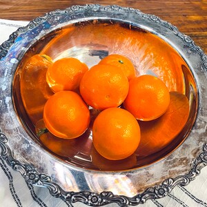 May include: A silver serving bowl with a decorative rim, filled with six bright orange oranges.