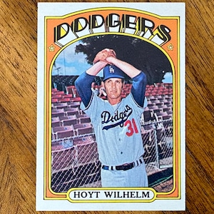 May include: A vintage baseball card featuring Hoyt Wilhelm in a grey Dodgers uniform with the number 31. The player is shown from the waist up with hands raised above the head. The card has an orange border with the text DODGERS and HOYT WILHELM.
