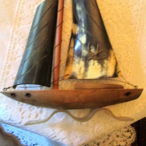 May include: A wooden sailboat wall decor with a black and white sail and a brown mast. The sailboat is on a white background.