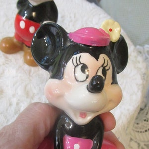 May include: A pair of vintage ceramic Mickey Mouse and Minnie Mouse figurines. Mickey is wearing red shorts with white polka dots and Minnie is wearing a pink dress with white polka dots and a pink hat with a white flower.