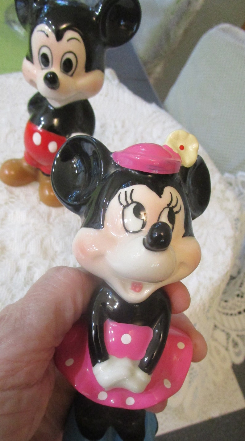 May include: A pair of vintage ceramic Mickey Mouse and Minnie Mouse figurines. Mickey is wearing red shorts with white polka dots and Minnie is wearing a pink dress with white polka dots and a pink hat with a white flower.