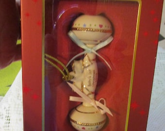 May include: A Lenox 2010 Annual baby rattle ornament in a red box. The cream-colored rattle features gold trim, small colorful hearts and stars, and a light pink ribbon. The text on the box reads 2010 ANNUAL and LENOX American by Design.