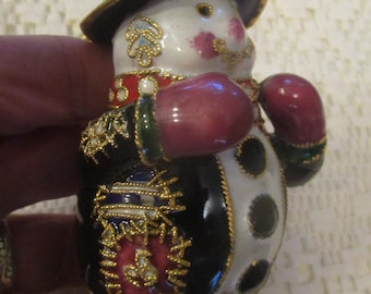 May include: A decorative snowman figurine with a black and white body, wearing a black hat and coat with gold accents. The snowman has red mittens and rosy cheeks, and is a festive holiday decoration.