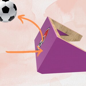 May include: A purple and wood soccer goal with a black and white target. A white and black soccer ball is flying towards the goal.