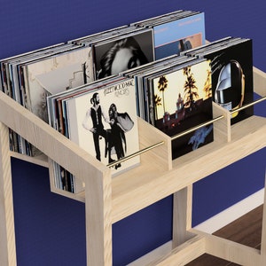 May include: A light wood record stand with a brass rail and multiple shelves to hold vinyl records. The stand is filled with records, including Fleetwood Mac's "Rumors" album.