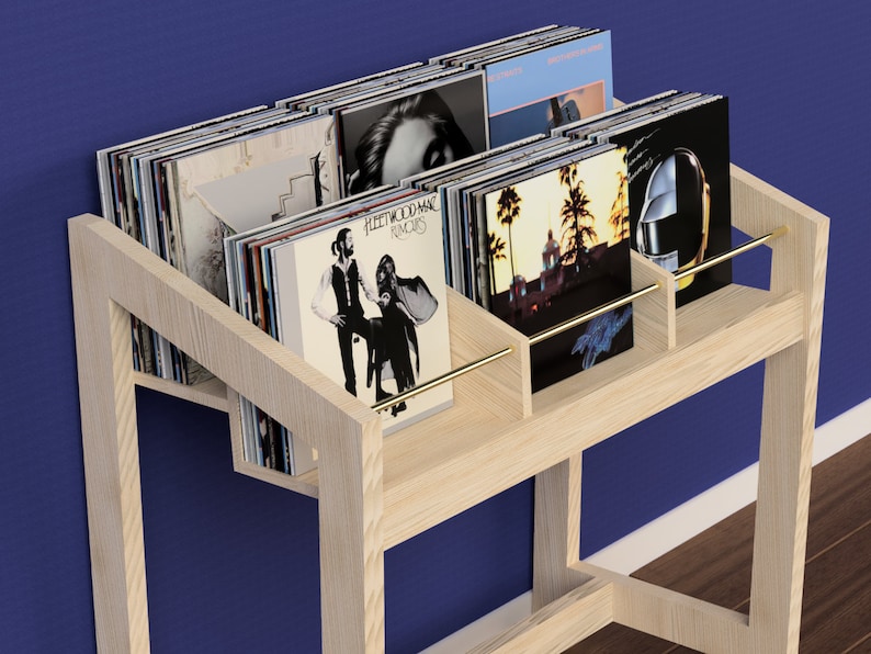 May include: A light wood record stand with a brass rail and multiple shelves to hold vinyl records. The stand is filled with records, including Fleetwood Mac's "Rumors" album.