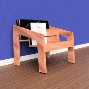 K&ouml;nnte beinhalten: Ein Holz-Plattenst&auml;nder mit zwei Regalen, auf denen ein Stapel Schallplatten liegt. Der St&auml;nder ist aus hellem braunem Holz gefertigt und hat ein schlichtes, modernes Design. Der Plattenst&auml;nder steht auf einem Holzboden vor einer blauen Wand.