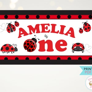 Pode incluir: Faixa de aniversário imprimível com tema de joaninha com bolinhas vermelhas e pretas. A faixa diz "Amelia faz um ano" em letras vermelhas.