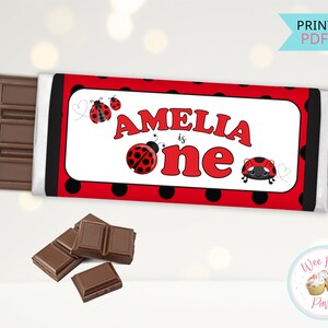 May include: Printable chocolate bar wrapper with a red and black polka dot pattern. The wrapper features a ladybug design and the text "Amelia is one".