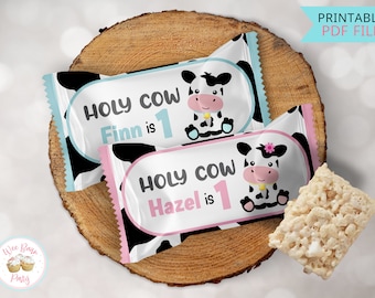 May include: Two printable favor bags with a cow design. The bags are white with black spots and feature a pink and blue cow with the text "Holy Cow" and the name "Finn" or "Hazel" followed by "is 1".