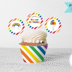Op de afbeelding: Printbare regenboog cupcake-verpakkingen en -toppers. De verpakkingen hebben een regenboogstrepenpatroon. De toppers bevatten een regenboog, ballonnen en de tekst "Happy Birthday!"