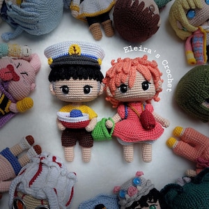 May include: A collection of handmade crochet dolls, including two central figures: a boy in a sailor hat and a girl in a pink dress. The dolls are surrounded by other crocheted figures in various colors and designs. The text "Eleira's Crochet" is visible.