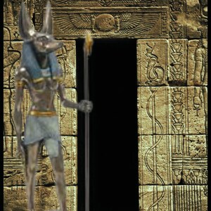 May include: A silver statue of an Egyptian god with a jackal head, standing in front of a stone doorway with intricate carvings. The god is holding a staff in his right hand.