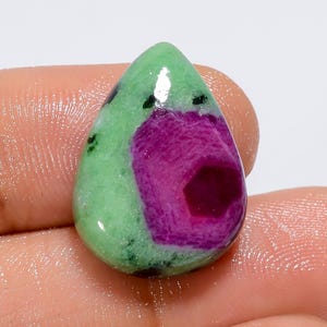 May include: A teardrop-shaped green and pink gemstone cabochon with a unique pattern. The stone has a green outer layer with a pink centre that has a darker pink hexagonal shape in the middle.