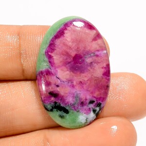 Puede incluir: Una gema ovalada con una paleta de colores vibrantes. La piedra presenta un área central de tonos rosa intenso y magenta, rodeada por una banda de verde claro. Las inclusiones negras y blancas añaden contraste.