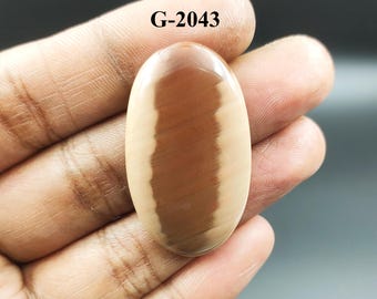 May include: A light brown and reddish-brown oval cabochon gemstone with a striped pattern. The gemstone is labeled "G-2043".