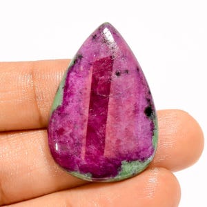 Op de afbeelding: Een druppelvormige edelsteen met een levendige mix van kleuren. De steen heeft een diep magenta centrum met strepen van lichter roze en zwarte vlekken. Groene tinten begrenzen de randen, wat een opvallend contrast creëert.