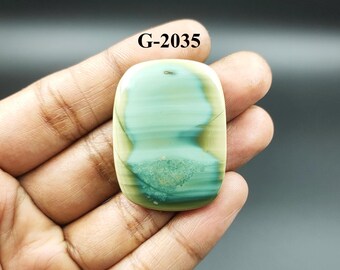May include: A green and beige cabochon gemstone with a striped pattern. The gemstone is oval-shaped and has a smooth, polished surface. G-2035