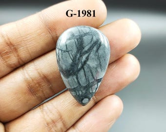 Könnte beinhalten: Ein grauer und schwarzer tropfenförmiger Cabochon-Edelstein mit einem wirbelnden Muster. Der Edelstein ist mit "G-1981" gekennzeichnet.