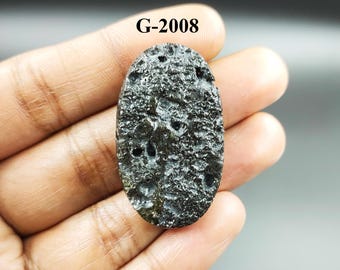 May include: A black oval-shaped stone with a rough, textured surface. The stone has a porous appearance with small holes throughout. The stone is labeled "G-2008".