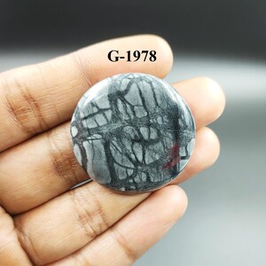 May include: A round, gray and black stone cabochon with a unique, intricate pattern. The stone has a polished, smooth surface. G-1978