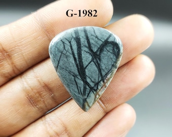 May include: A gray and black gemstone cabochon with a unique pattern, shaped like a guitar pick. The stone is labeled "G-1982".