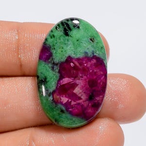 Op de afbeelding: Ovaalvormige groene en roze edelsteen cabochon met een gevlekt patroon. De steen heeft een glad, gepolijst oppervlak.