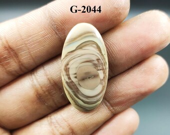 May include: A close-up of a light brown, oval-shaped, polished stone with a swirling pattern of light and dark brown lines. The stone is labeled "G-2044".