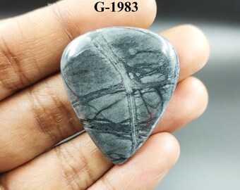 May include: A gray and black gemstone cabochon with a teardrop shape. The stone has a unique pattern of black lines and swirls. The stone is labeled G-1983.