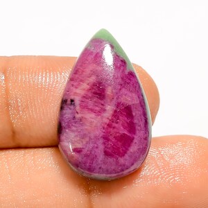 Op de afbeelding: Een gepolijste, druppelvormige edelsteen met een levendig roze en rood interieur en een groene top. Het oppervlak van de steen toont natuurlijke patronen en kleurvariaties. Deze unieke edelsteen is ideaal voor sieraden.