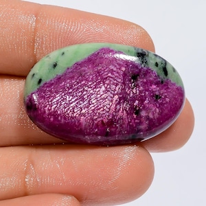 Op de afbeelding: Ovaalvormige groene en roze edelsteen cabochon met zwarte vlekken.