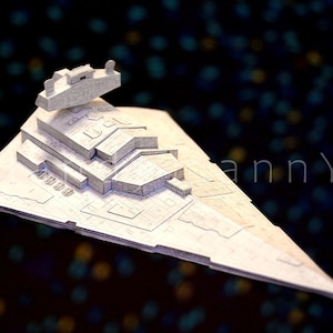 May include: A detailed, light gray model of a Star Destroyer spaceship, featuring intricate surface details and a prominent command tower. The model is set against a dark background with blurred, colorful lights, suggesting a space theme.